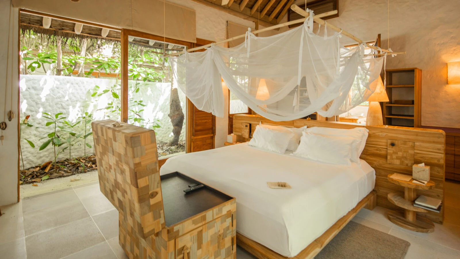 Quarto de uma villa do Soneva Fushi com madeira natural e portas abertas para a vegetação